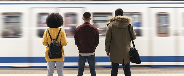 Three people stand waiting for a train