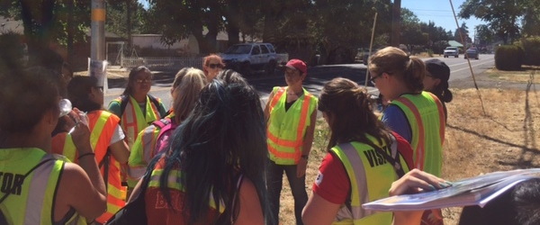 Students in reflective jackets with clipboards standing near a sidewalk