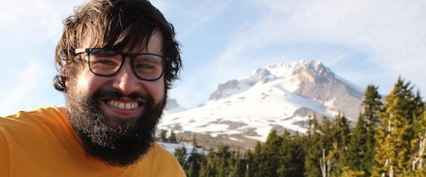 Jaime Orrego-Onate, wearing glasses and an orange T-shirt, faces the camera with a mountain in the background.