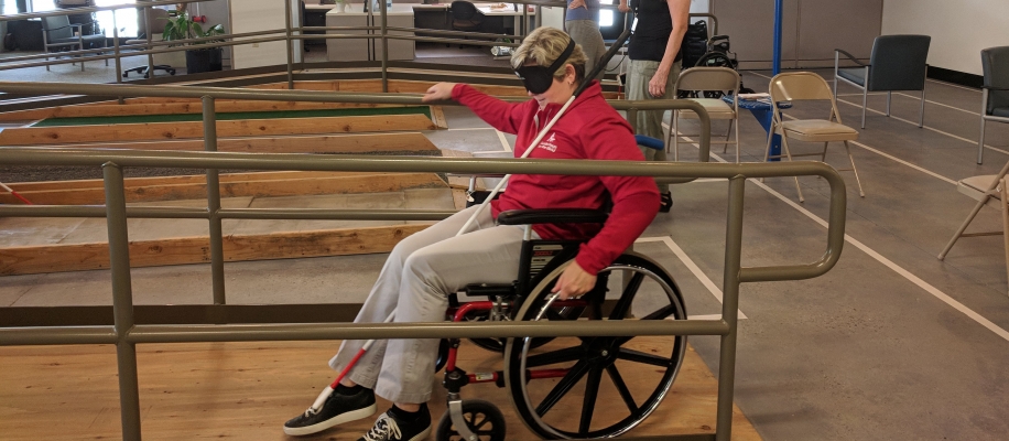A blindfolded woman navigates a wheelchair up a ramp