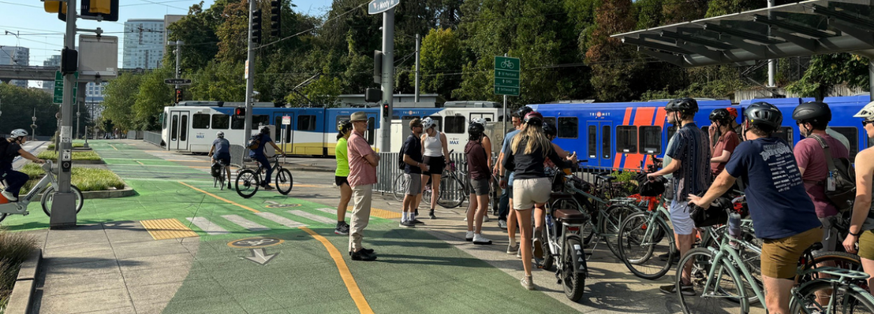 Bikeway design workshop participants on bikes, listening to an instructor during a field tour.