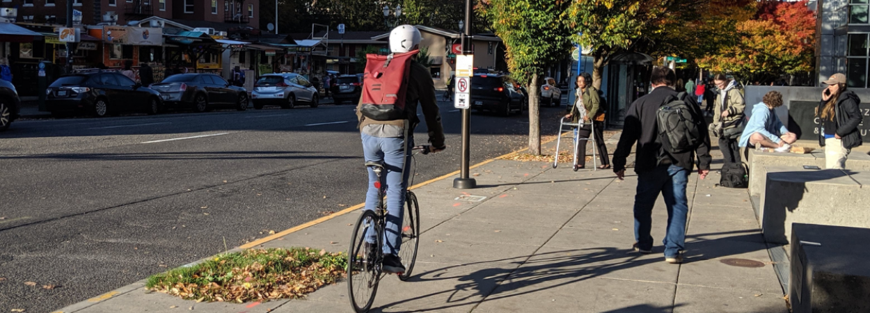 Bicyclists and pedestrians, including one person using a walker or mobility device, navigate the PSU campus.