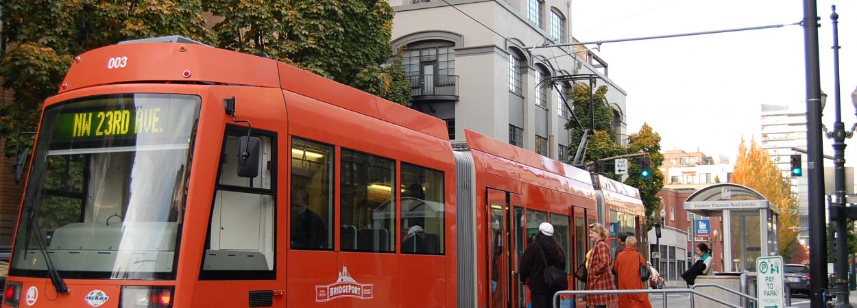 A red Portland streetcar waits at a stop for riders to board.
