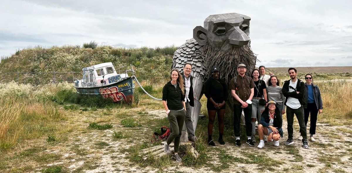 A group of students and instructor John MacArthur standing near a large troll, which towers above them nearly twice their height. It has a long beard, a bald head, and a benign facial expression.